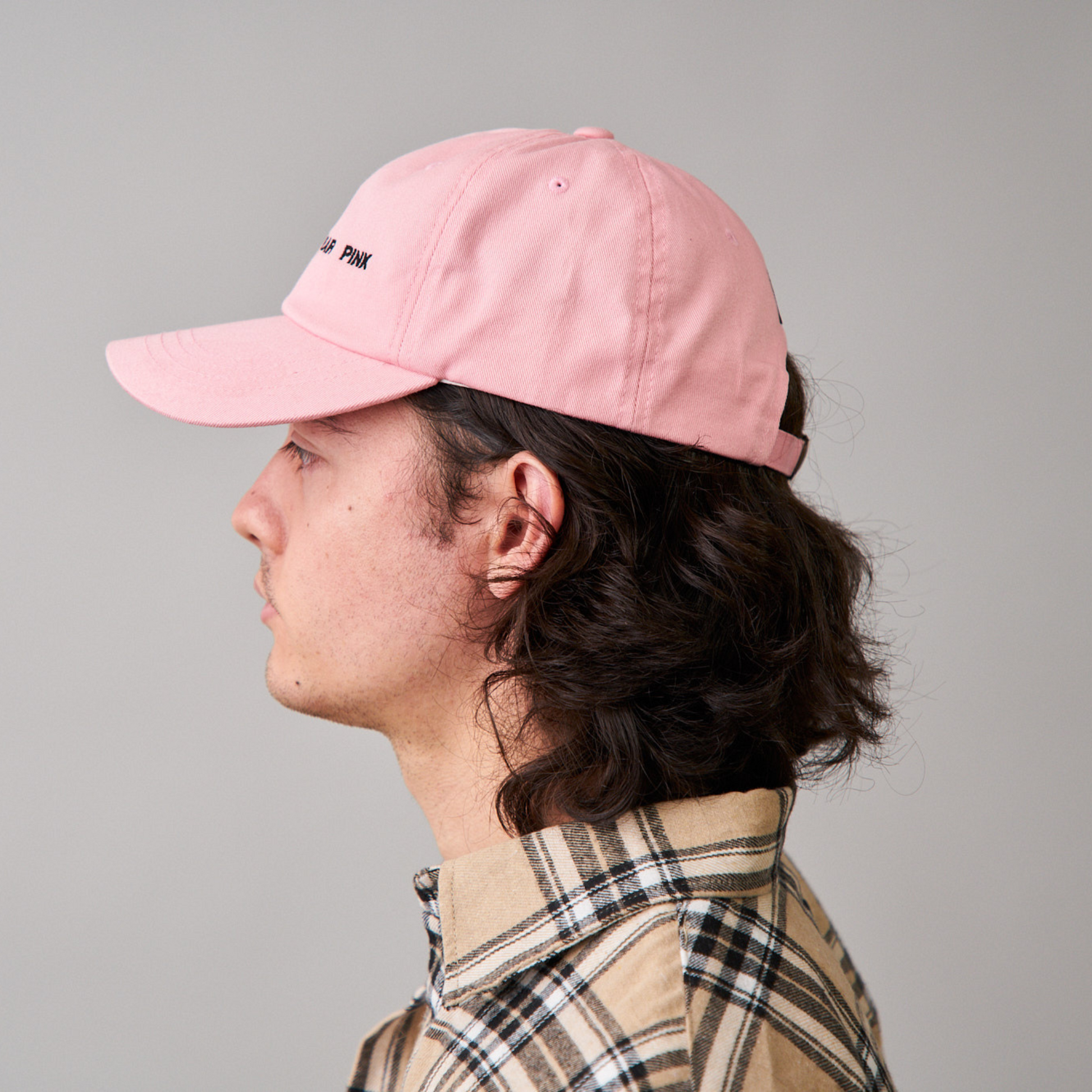 side view of man wearing a pink dad cap with'REAL MEN WEAR PINK' printed on the front, paired with a beige flannel shirt, featuring DUUW WUUD's stylish and causal wear.