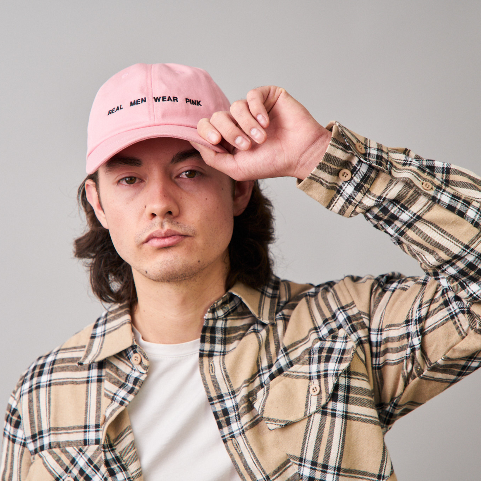 Man wearing a pink dad cap with 'REAL MEN WEAR PINK' printed on the front, paired with a beige flannel shirt, featuring DUUW WUUD's stylish and casual wear.