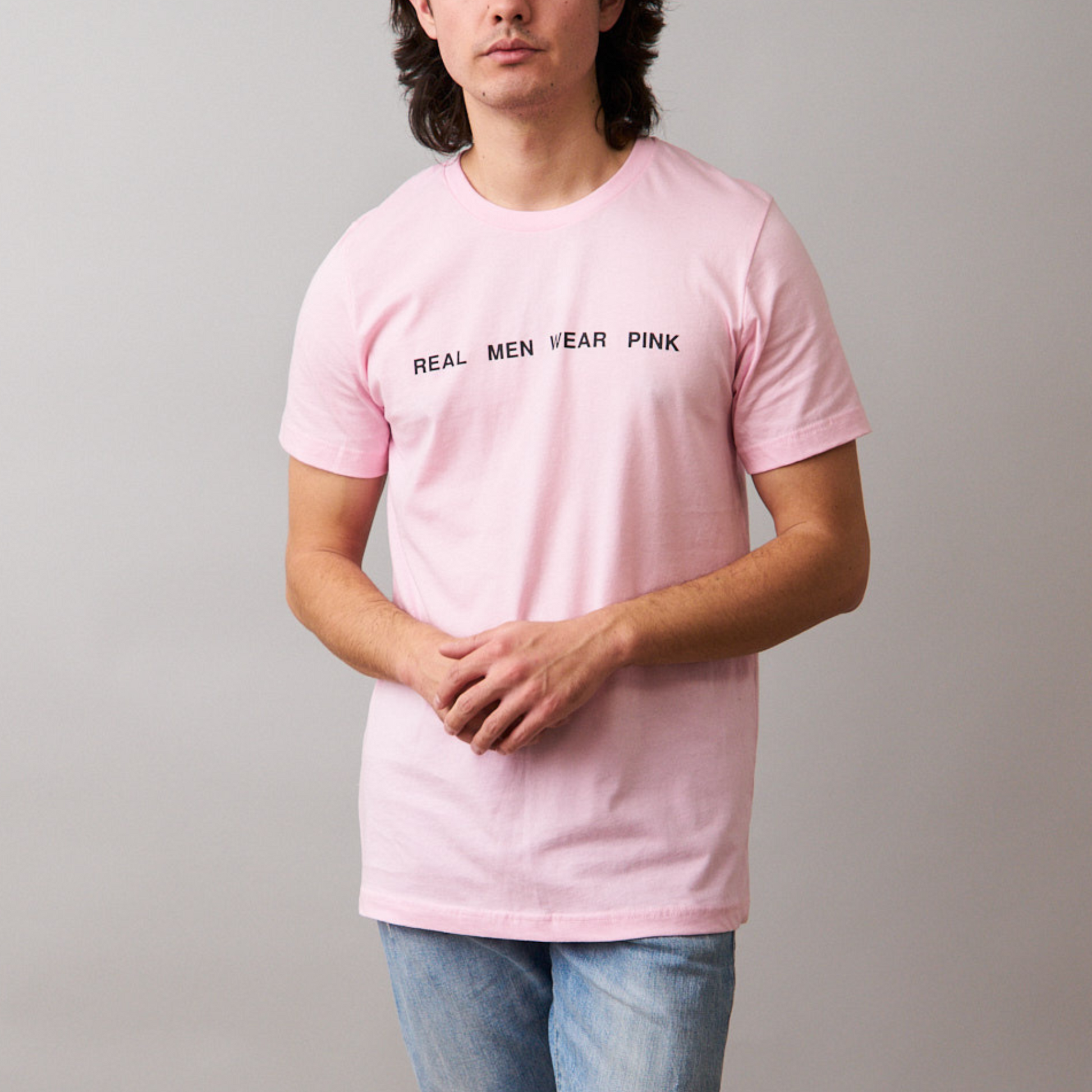 Man wearing a pink t-shirt with 'REAL MEN WEAR PINK' printed on the front, paired with blue jeans.