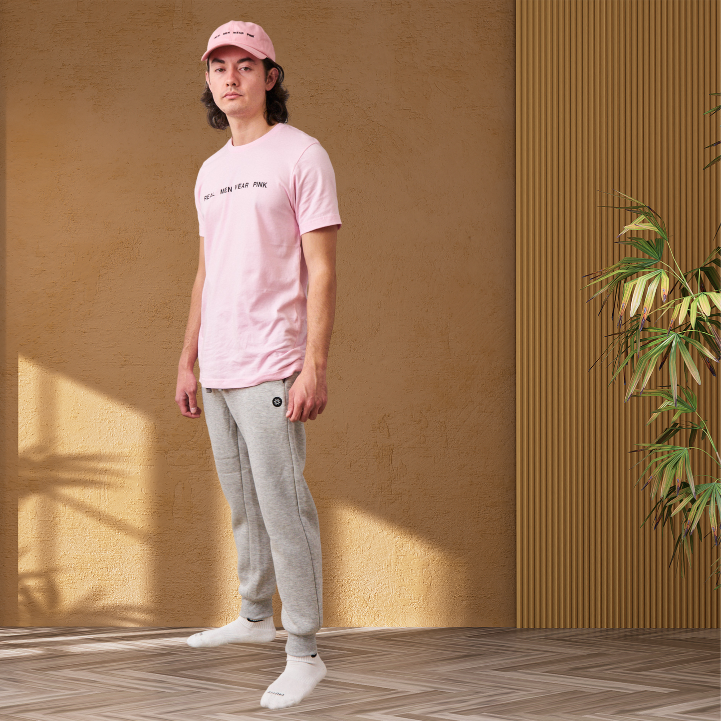 Man wearing gray fleece jogger sweatpants with ribbed bottom cuffs. The joggers have a tapered slim fit and a drawstring waistband, paired with a pink t-shirt and pink dad cap, both featuring 'REAL MEN WEAR PINK' printed on the front. 